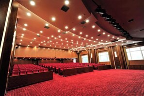 A large auditorium with rows of red seating, a carpeted floor, and a high ceiling with recessed lighting.
