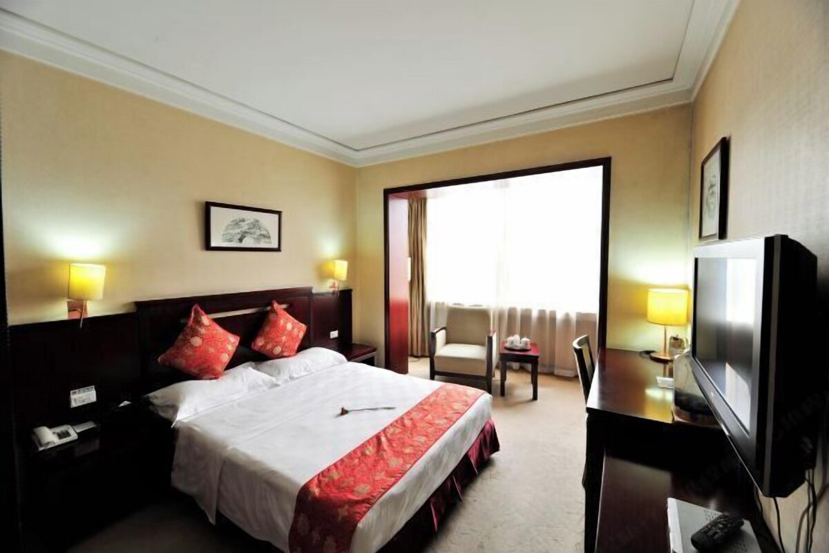 A hotel room with a bed, bedside lamps, a television, a desk, and a chair.