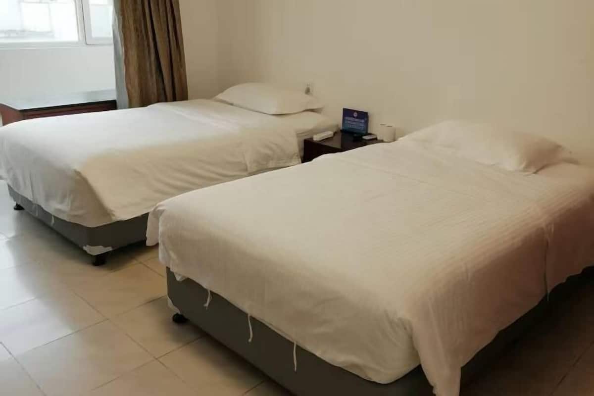 A hotel room with two beds, a nightstand, and a window with curtains.