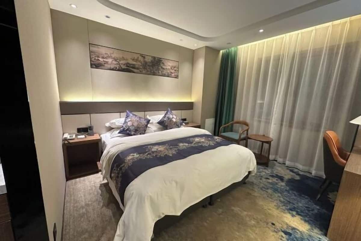 A modern hotel room with a large bed, a nightstand, a chair, and a desk.