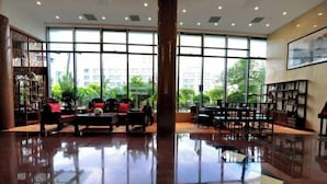 A spacious lobby with a polished floor, large windows offering a view of greenery, and a traditional wooden screen on the left. - Beijing Post & Telecom Conference Centre (Beijing)