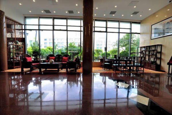 A spacious lobby with a polished floor, large windows offering a view of greenery, and a traditional wooden screen on the left. - Beijing Post & Telecom Conference Centre (Beijing)