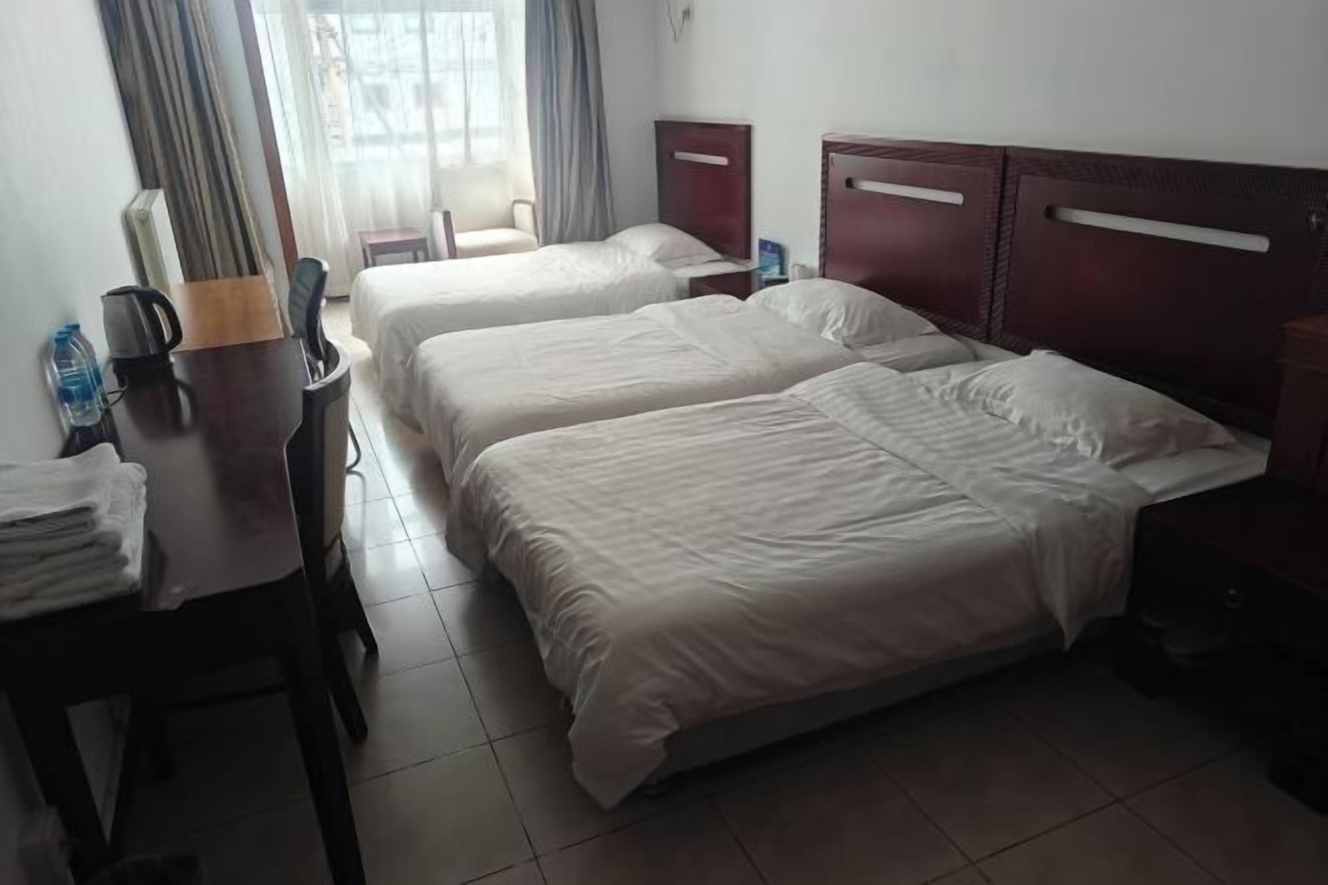Una habitación de hotel con dos camas, un escritorio con silla, una mesita y una ventana con cortinas.