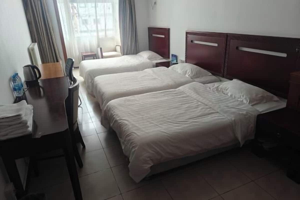A hotel room with two beds, a desk with a chair, a small table, and a window with curtains.