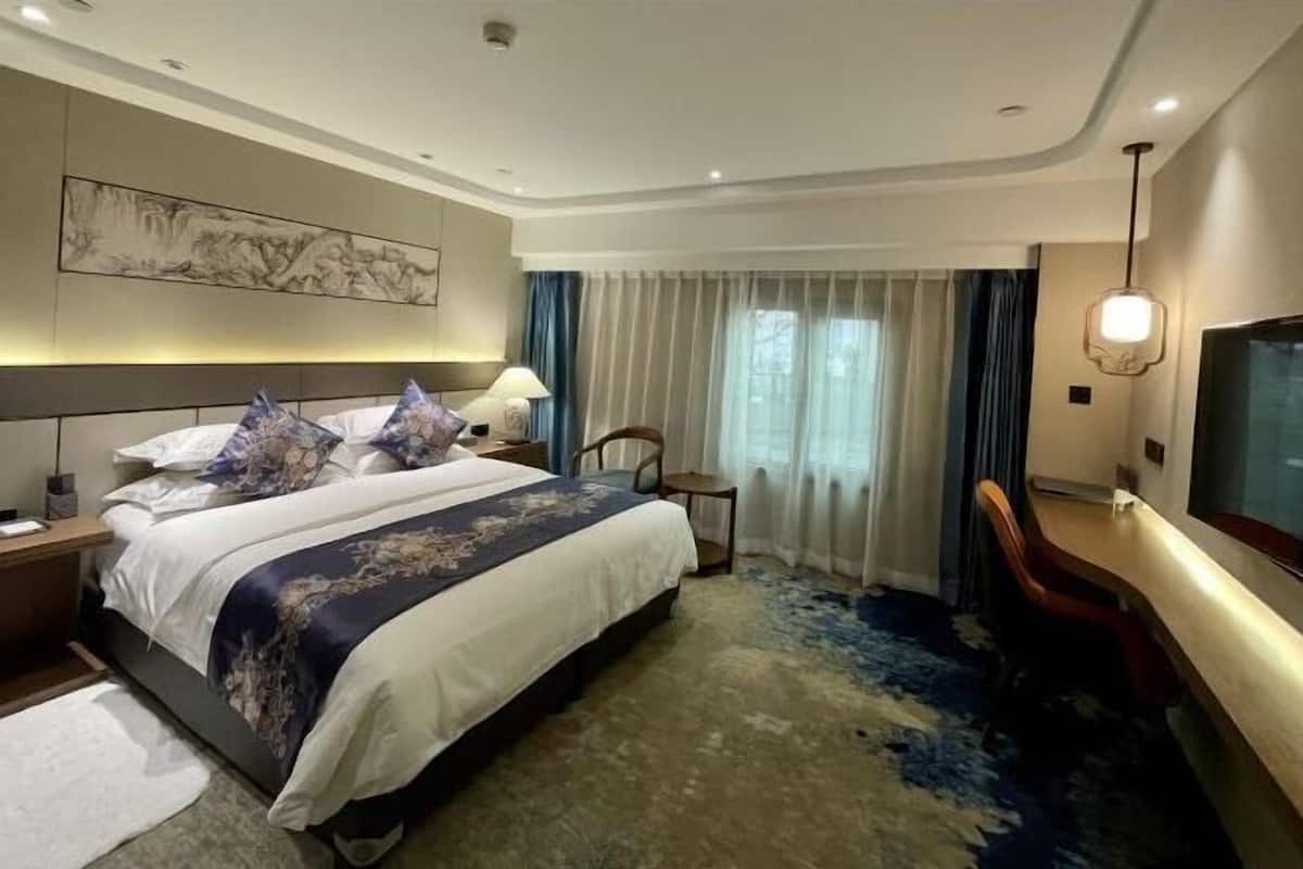 A hotel room with a large bed, a desk, a chair, a TV, and a painting on the wall.