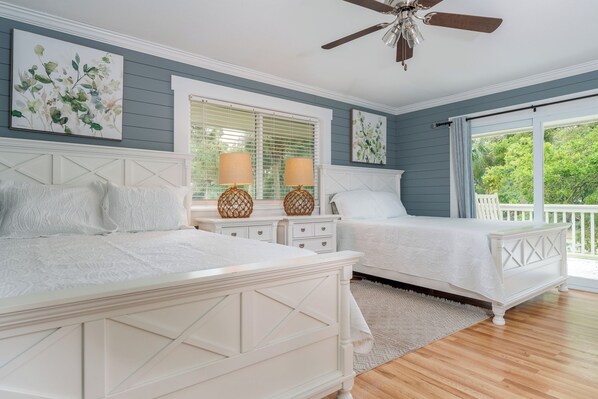 A bedroom with two beds, a ceiling fan, and a view of the outdoors.
