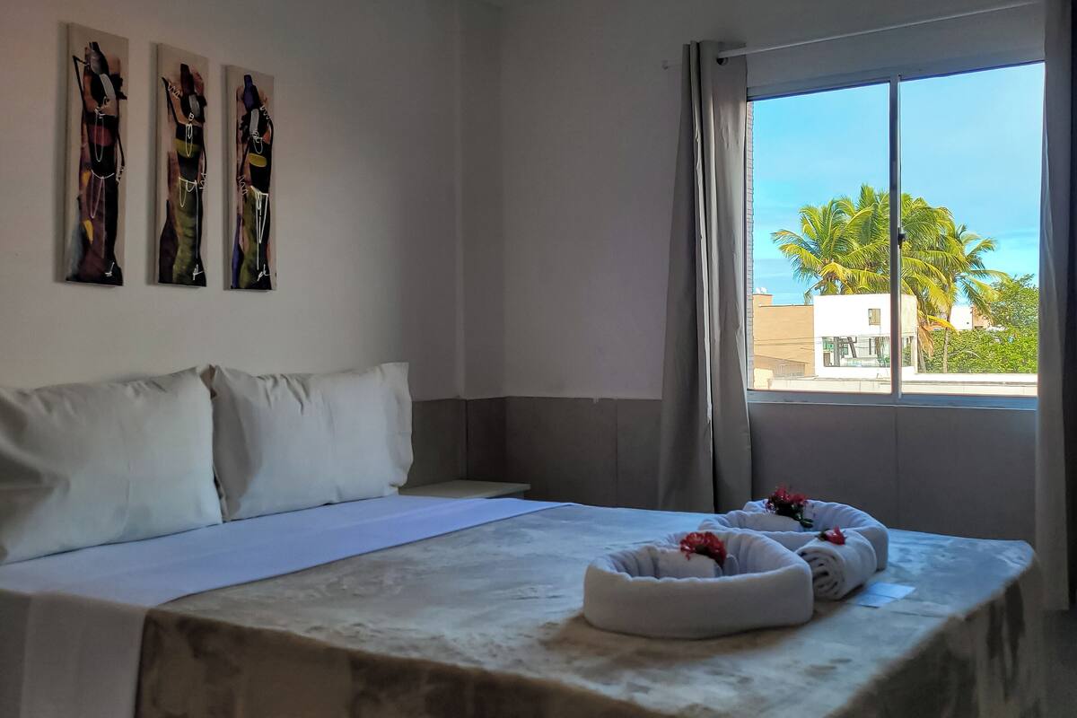 Habitació d'hotel amb un llit, almoines blanques, una finestra gran i tres obres d'art a la paret.