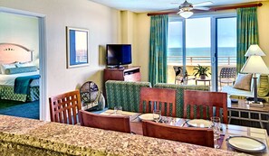 Una habitación de hotel con balcón, televisión, zona de comedor y cama.