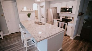 Cozinha moderna com bancada de granito, eletrodomésticos de aço inoxidável e uma ilha central com banquetas.