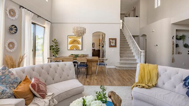 A spacious living room with a high ceiling, a staircase, and a dining area.