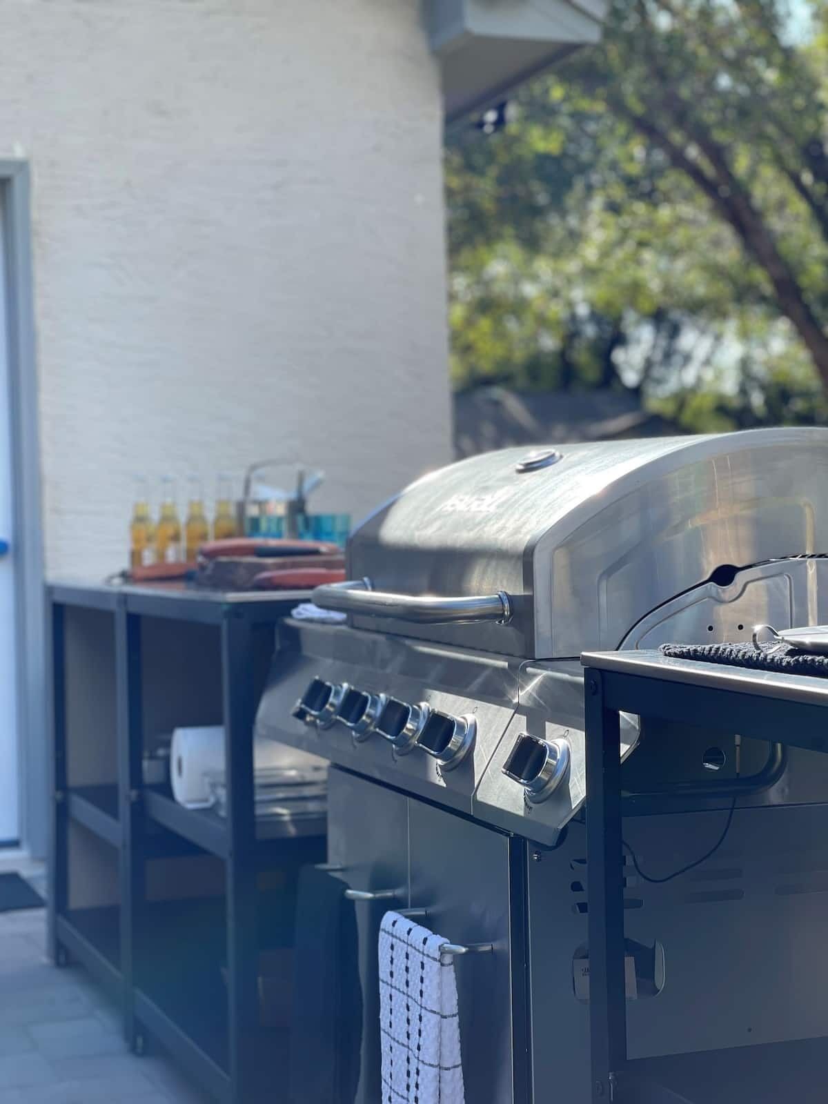 A stainless steel barbecue grill with multiple burners, a built-in thermometer, and a side table with condiments.
