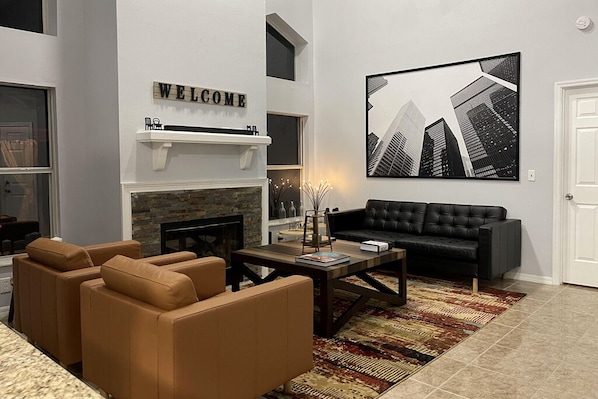 A modern living room with a fireplace, a black leather sofa, and a cityscape painting on the wall.