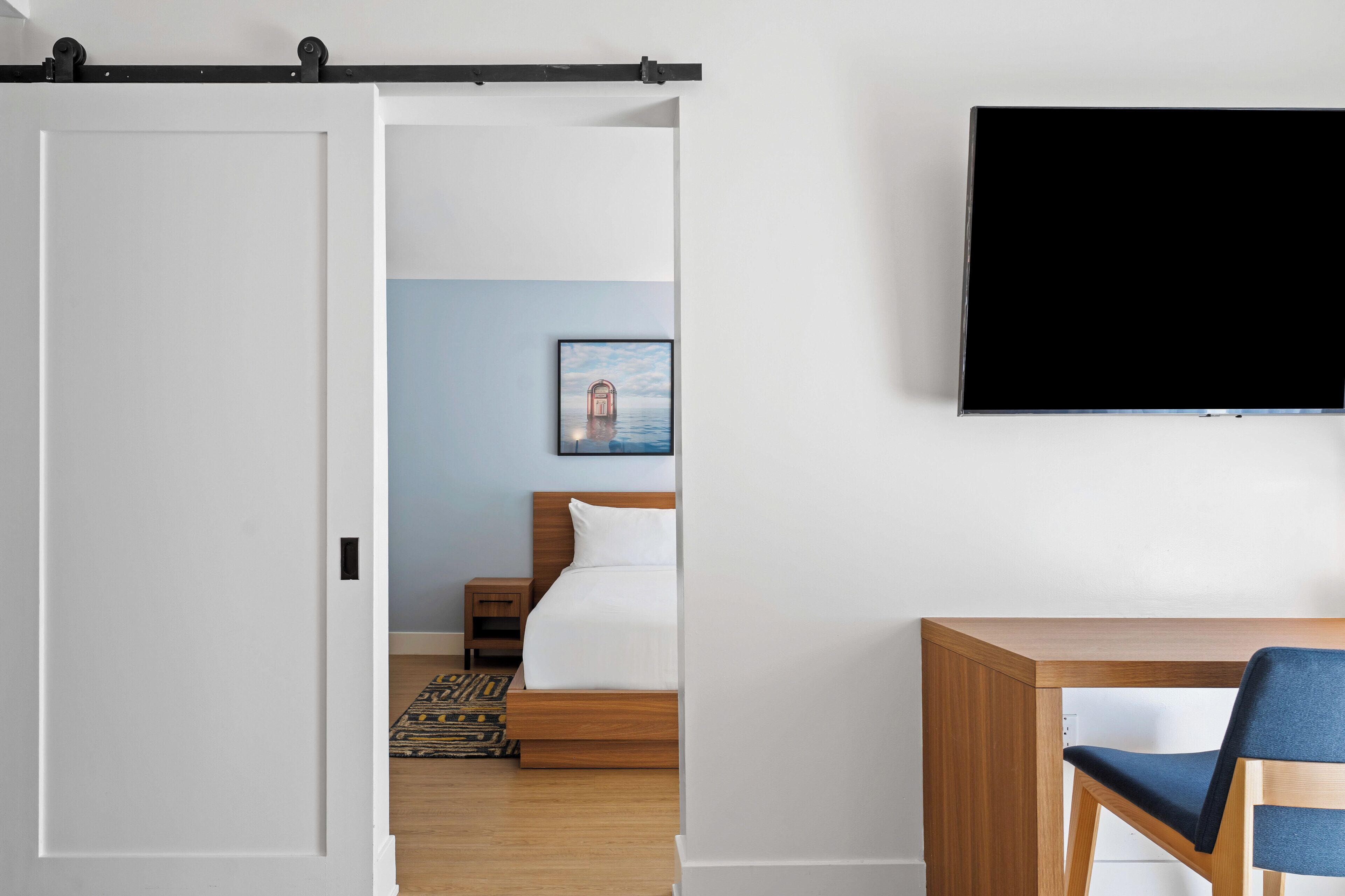 A hotel room with a bed, a desk, a chair, a TV, and a picture on the wall.