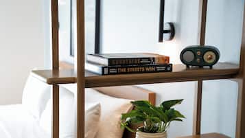 A wooden shelf with books and a radio, a potted plant, and a bed with white bedding.