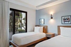 Une chambre d’hôtel avec deux lits, une table de chevet, une lampe fixée au mur et une fenêtre donnant sur un paysage verdoyant.