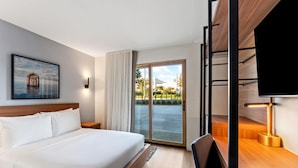 A hotel room with a bed, a desk with a lamp, a TV, a window with curtains, and a painting on the wall. - The Anthem Los Angeles Stadium District, Tapestry by Hilton (Inglewood)