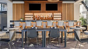 Un área de bar moderna con lámparas colgantes de mimbre, paneles de madera y una variedad de botellas y vasos en estantes.