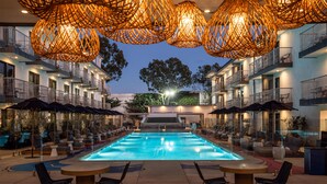 Una piscina con sillas de descanso y sombrillas, rodeada por un edificio con balcones y zonas de estar al aire libre.