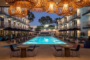 A swimming pool with lounge chairs and umbrellas, surrounded by a building with balconies and outdoor seating. - The Anthem Los Angeles Stadium District, Tapestry by Hilton (Inglewood)