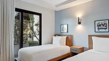 Habitación de hotel con dos camas, una ventana que da a zonas verdes, una lámpara de pared e imagen enmarco.
