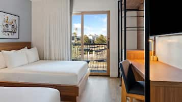 A hotel room with a bed, a desk, and a view of the city.
