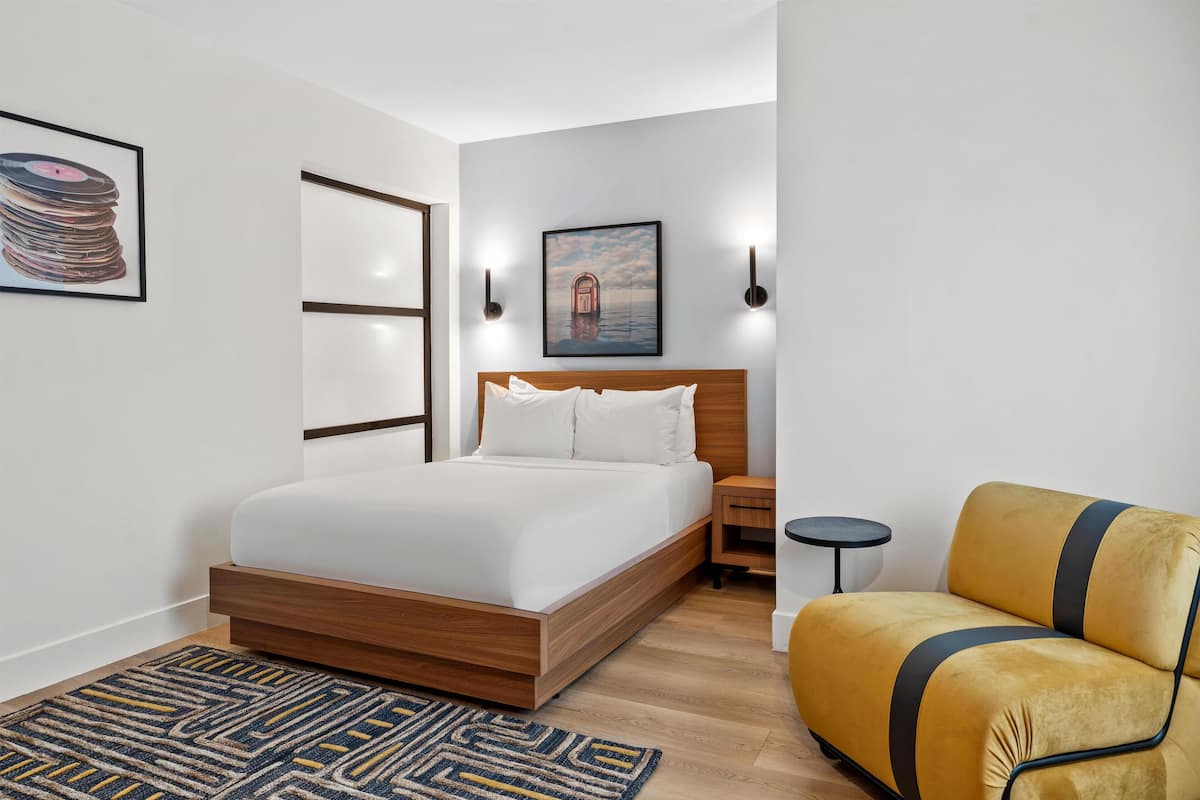 Un dormitorio moderno con una cama de madera, un sofá amarillo, una mesita redonda y un cuadro en la pared.