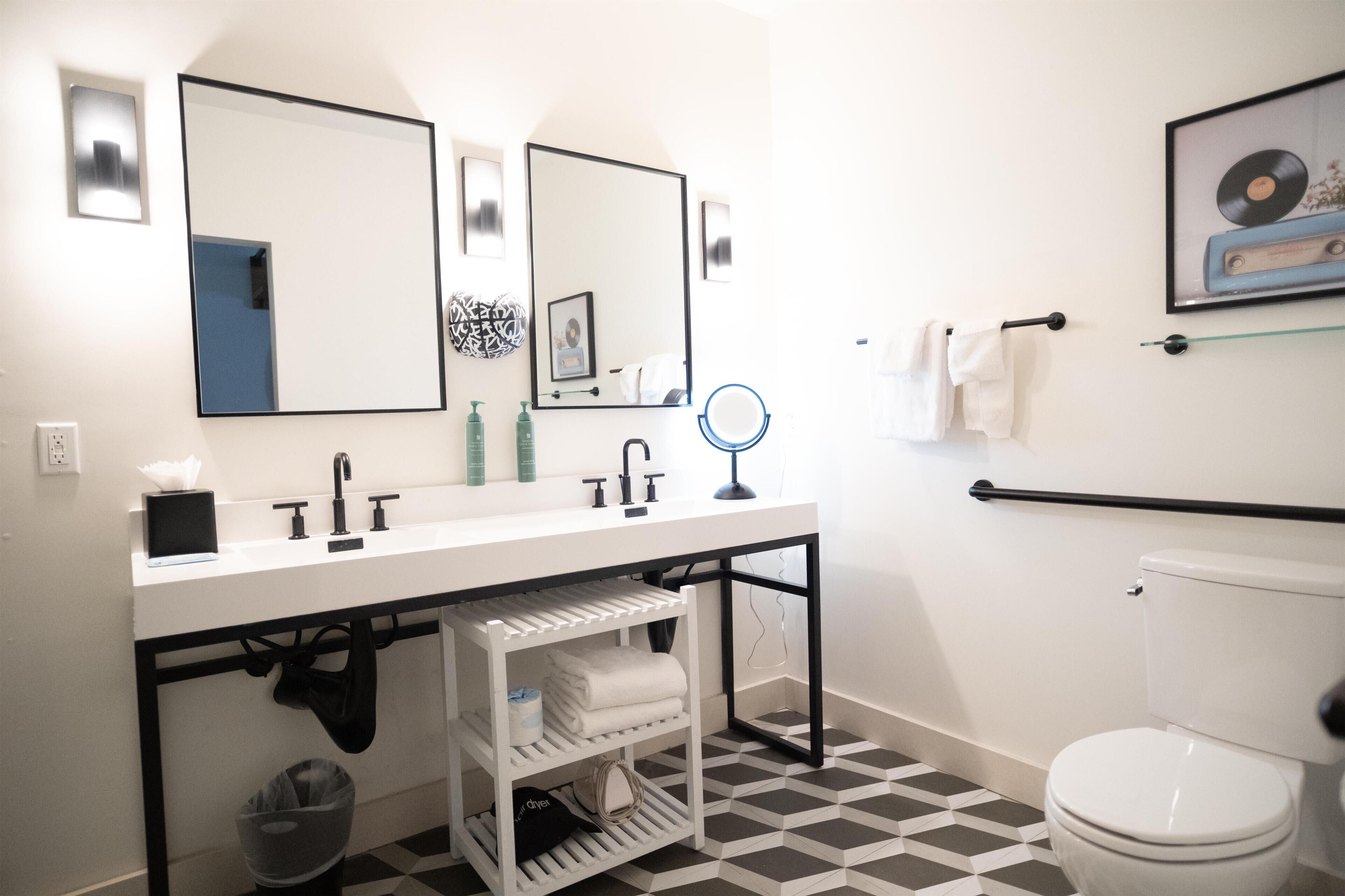 A modern bathroom with a white sink, two mirrors, a toilet, and a patterned floor.
