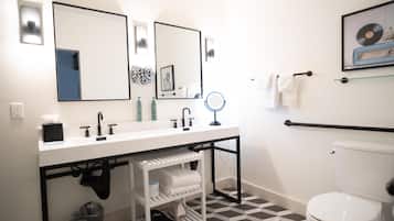 A modern bathroom with a white sink, two mirrors, a toilet, and a patterned floor.