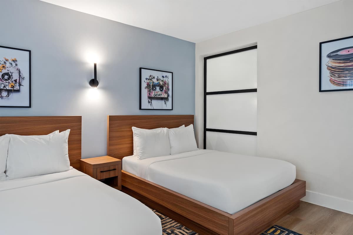 Una habitación de hotel moderna con dos camas individuales, un cabecero de madera, una mesita de noche y una lámpara fijada a la pared.