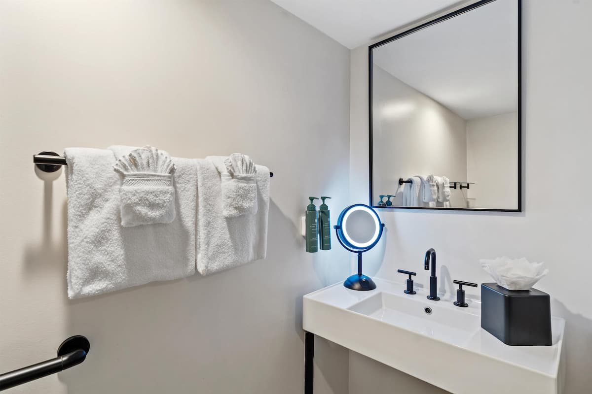 Un baño con un lavamanos blanco, un espejo con luz y dos toallas colgadas en un perchero.