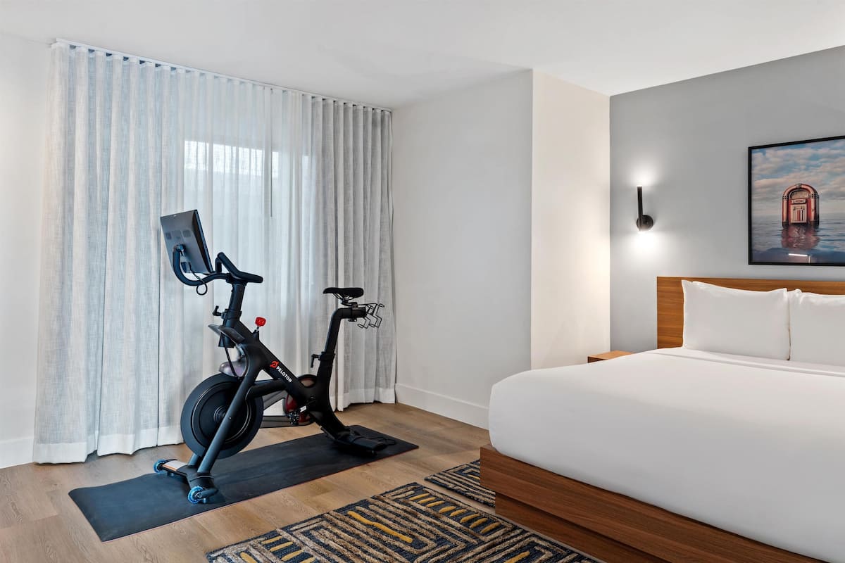 Habitación de hotel con cama, bicicleta estática y un ventanal con cortinas.