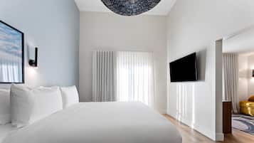 A modern hotel room with a large bed, a flat-screen TV mounted on the wall, and a view of the outdoors through the window.