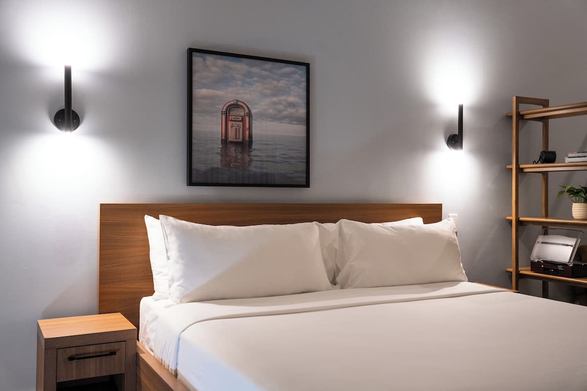 Una cama bien hecha con sábanas blancas, un cabecero de madera y dos lámparas de lectura fijadas a la pared.
