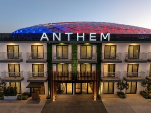Een hotel met een modern design, voorzien van balkons met leuningen, een opvallende entree met een houten poort en een groot verlicht bord boven de entree.