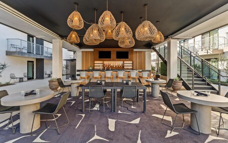 A modern outdoor dining area with round tables and chairs, a bar with stools, and a staircase leading to an upper level.