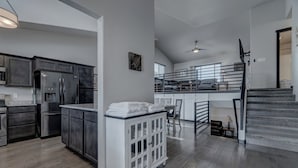 A spacious kitchen with dark cabinetry, a central island, and a dining area with a high ceiling and a staircase. - Convenient Location Family-Friendly Locally Owned (Rapid City)