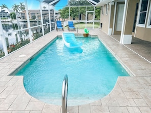 Una piscina con agua cristalina azul, rodeada por un deck de baldosas y un cerramiento de vidrio.