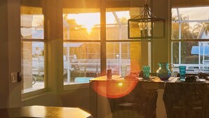 Un espace repas comprenant une table et des chaises, un luminaire suspendu et de grandes fenêtres donnant sur l’extérieur.