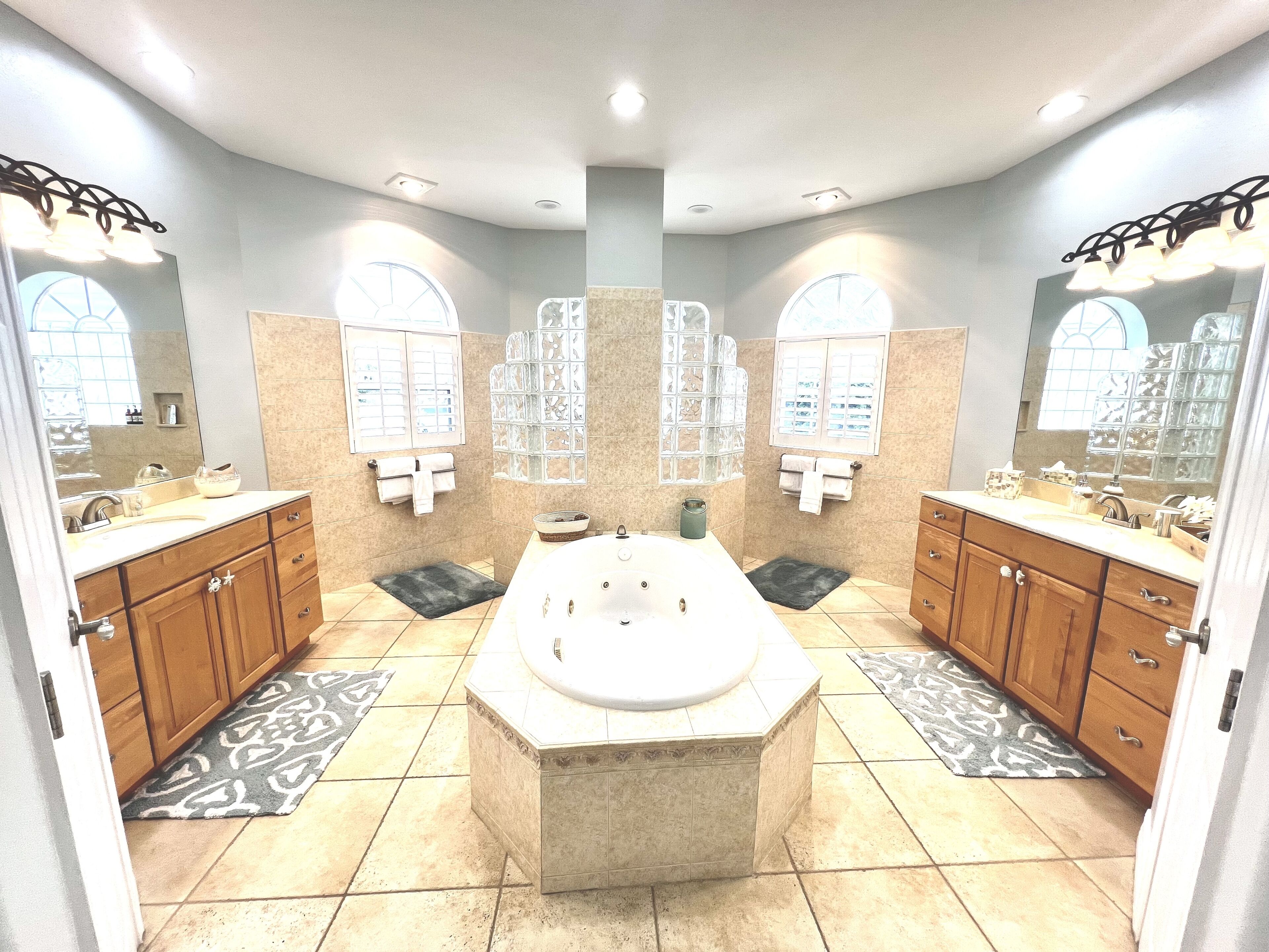 A spacious bathroom with a large central bathtub, double sinks, and a vanity with a mirror.