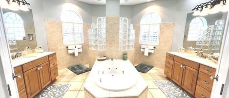 A spacious bathroom with a large central bathtub, double sinks, and a vanity with a mirror.