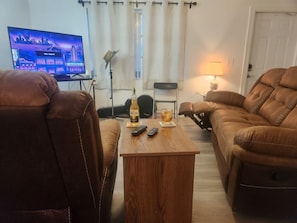Una sala de estar con sofás de cuero, una mesa de centro de madera, un televisor que muestra un paisaje urbano, una guitarra y una lámpara.