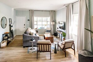 A living room with a sofa, coffee table, and chairs, a television, and a window with curtains.