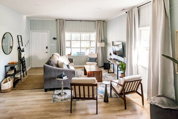 A living room with a sofa, coffee table, and chairs, a television, and a window with curtains.