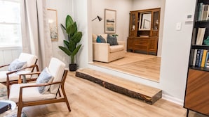 A modern living room with a sofa, armchairs, a wooden cabinet, and a large plant. - Sea Salt Cottage: Your Tranquil Getaway 3 min to beach (Cape Charles)