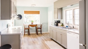 A modern kitchen with a dining table, chairs, and a window with blinds. - Sea Salt Cottage: Your Tranquil Getaway 3 min to beach (Cape Charles)