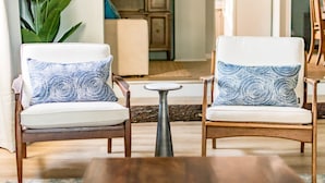 Two armchairs with patterned cushions, a small round table, and a large plant in a well-lit room with wooden flooring and a cabinet in the background. - Sea Salt Cottage: Your Tranquil Getaway 3 min to beach (Cape Charles)