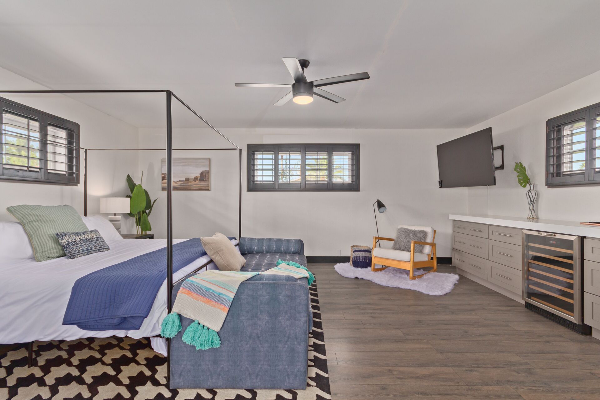 A modern bedroom with a bed, a sofa, a desk, and a ceiling fan.