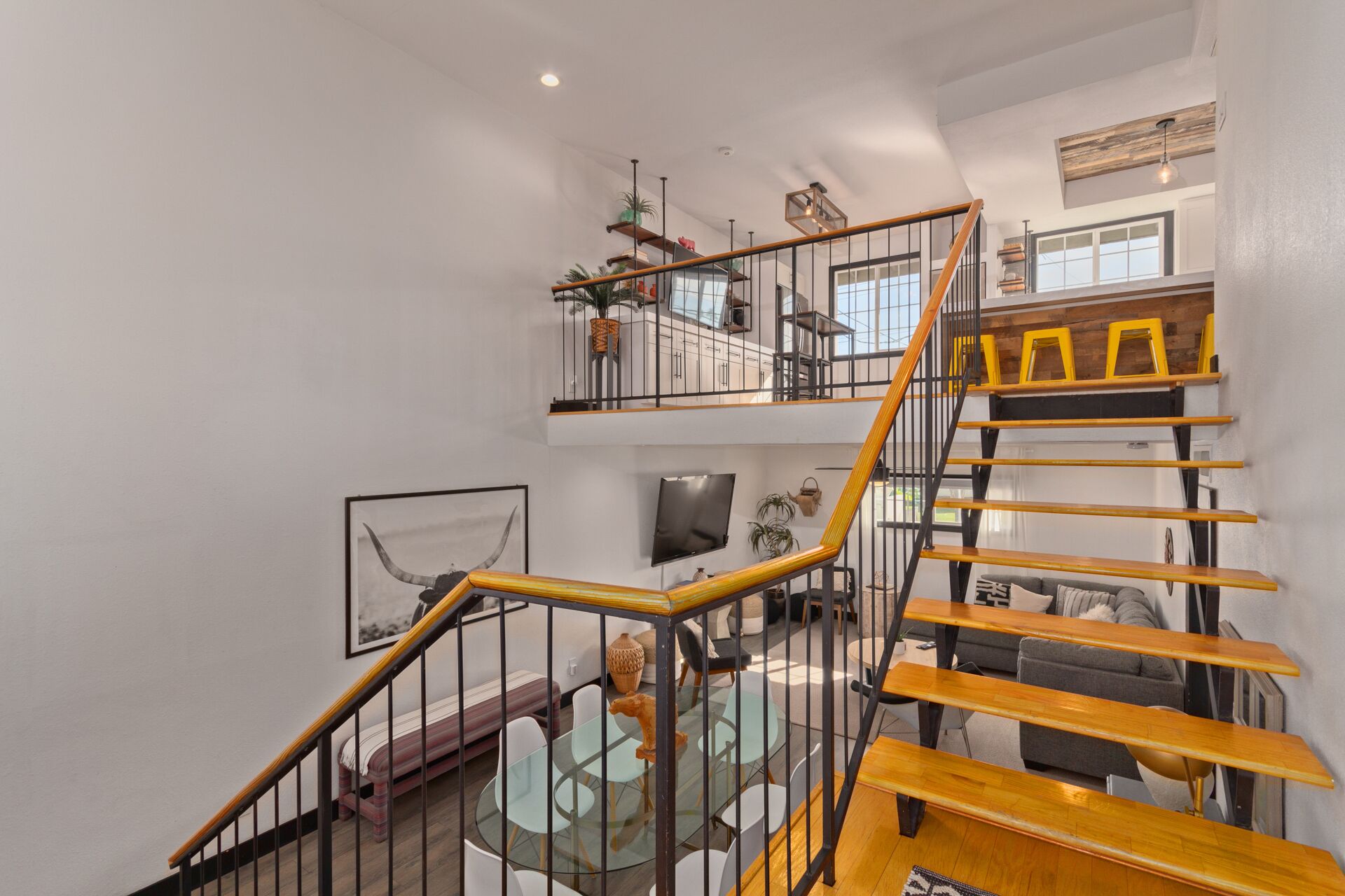 A multi-level interior with a wooden staircase, glass tables, and a TV mounted on the wall.