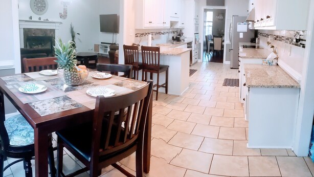Uma cozinha ampla com armários brancos, uma ilha central e um espaço de jantar com mesa e cadeiras de madeira.