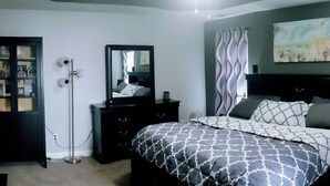 Um quarto com uma cama, cômoda, espelho, televisão e um quadro na parede.